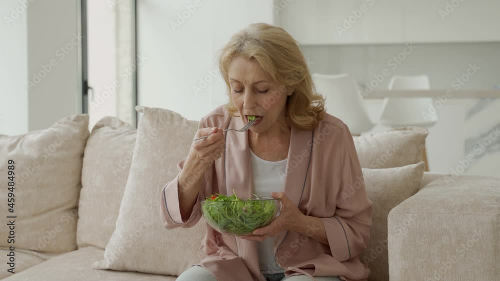 Beautiful elderly woman eats her vegetable salad sitting at home on the couch Beautiful elderly woman eats her vegetable salad sitting at home on the couch