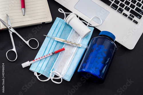 Φωτογραφία on a black background is a laptop, notebook, pen, pills, syringes, masks, drops,