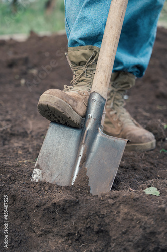 Farmer's feet shod in boots dig the ground with a shovel, vertical photo