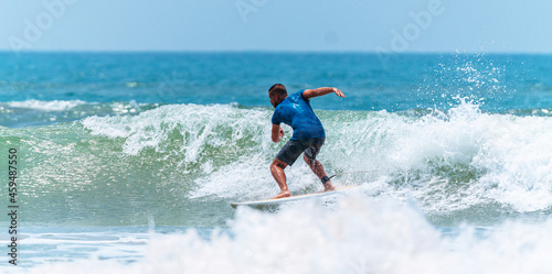 Mężczyzna surfer płynący na fali na tle błękitnego oceanu i nieba. © insomniafoto