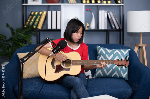 Happy cheerful pretty smiling of portrait a Asian girl vocalist with a Guitar recording a song front of microphone in living room.