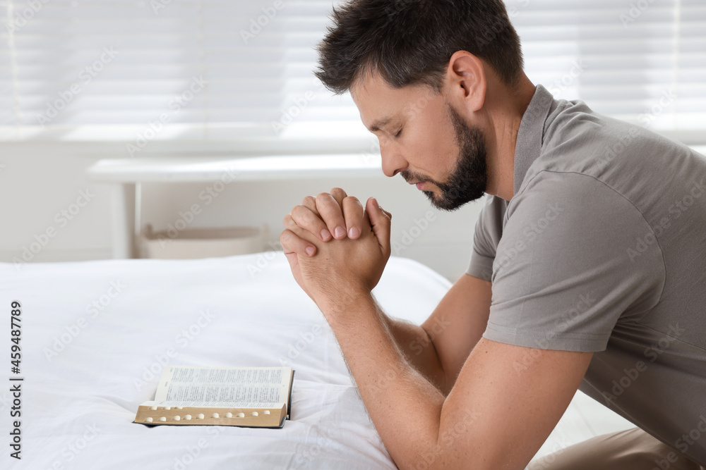 Obraz premium Religious man with Bible praying in bedroom