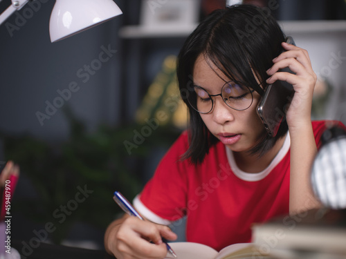 Asian girl talking on cell phone and taking notes in the room.
