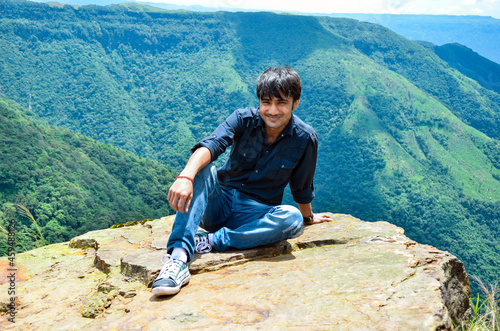 Long shot of a young man sitting at the edge of a mountain cliff, 4500 feet above from the ground