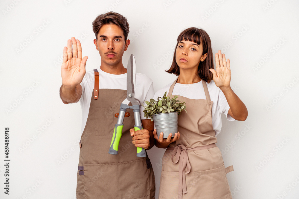Young mixed race gardener couple isolated on white background standing with outstretched hand showing stop sign, preventing you. Young mixed race gardener couple isolated on white background standing with outstretched hand showing stop sign, preventing you.