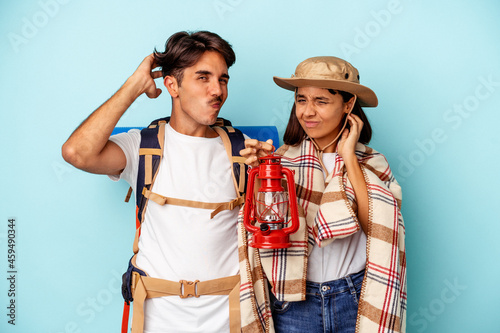 Young mixed race hiker couple isolated on blue background touching back of head, thinking and making a choice.