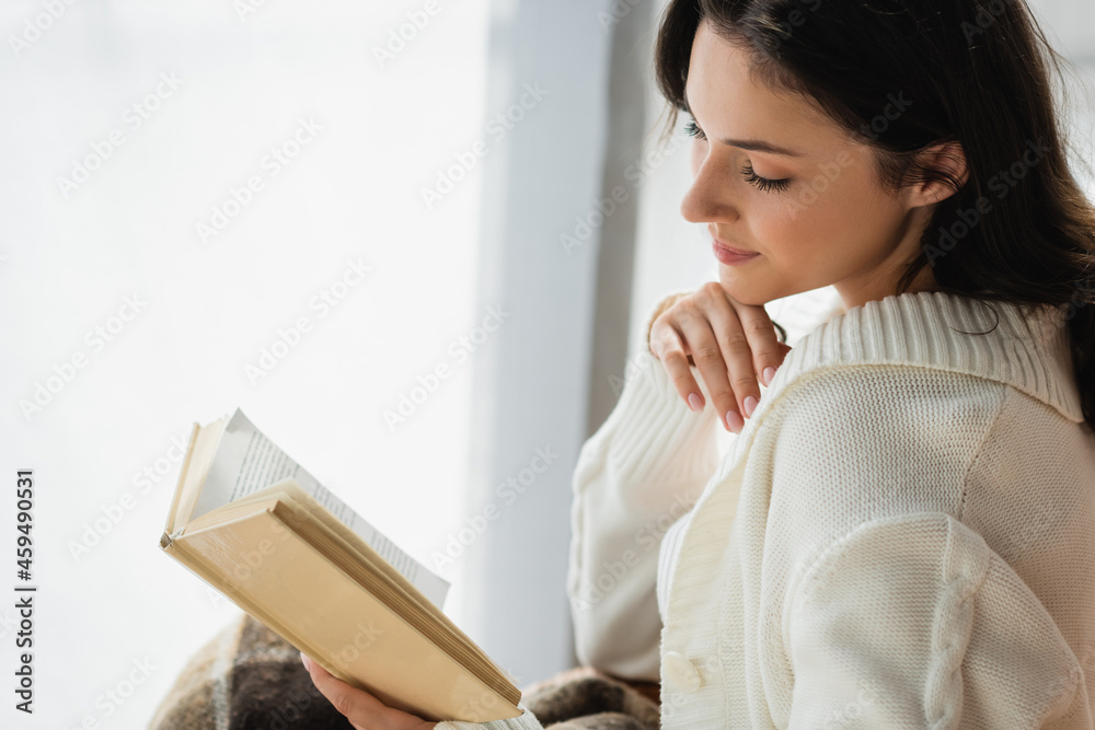 young woman in knitted cardigan reading novel at home young woman in knitted cardigan reading novel at home