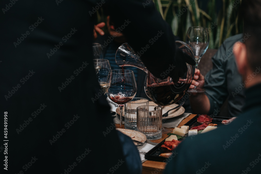 Elegant waiter pours red wine from bottle into glass at restaurant. Sommelier tasting wine in restaurant. Copy space for text menu elegant or recipe on dark background.