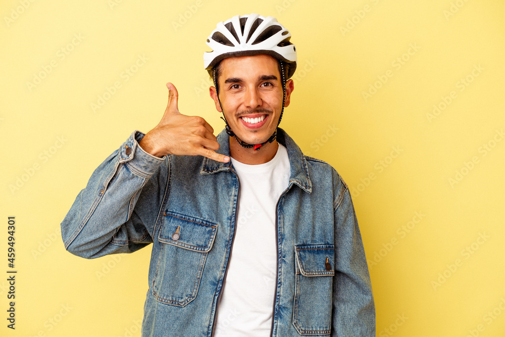 Young mixed race man wearing a helmet bike isolated on yellow background showing a mobile phone call gesture with fingers.
