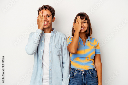 Young mixed race couple isolated on white background having fun covering half of face with palm.