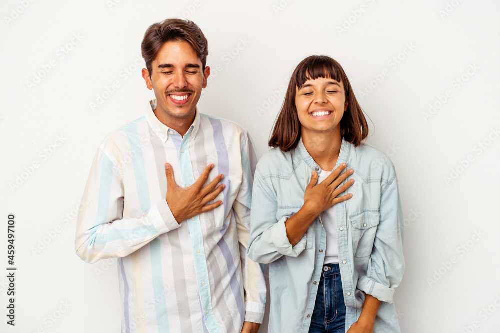 Young mixed race couple isolated on white background laughs out loudly keeping hand on chest. Young mixed race couple isolated on white background laughs out loudly keeping hand on chest.