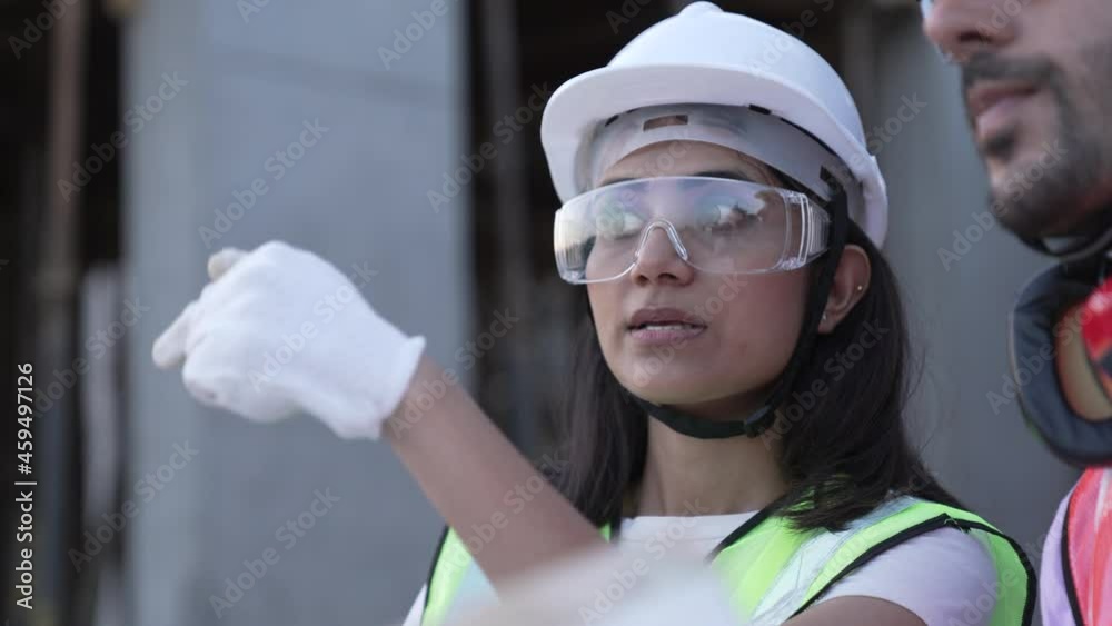 Close up of Indian workers people wearing protective safety helmet and glasses on construction site.Male and female engineers holding drawing plan working on construction side discussing about project
