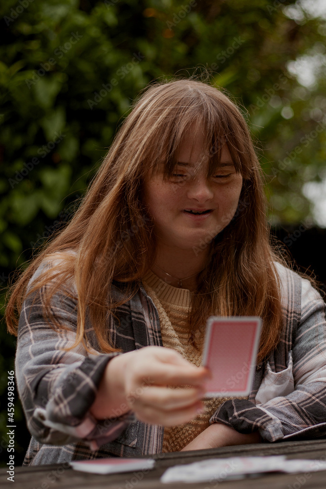Young woman with Down Syndrome playing cards outdoors and looking confident Young woman with Down Syndrome playing cards outdoors and looking confident