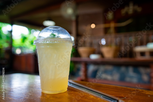 Lemon soda is placed in a plastic cup with a straw on a wooden table in a canal-side restaurant.