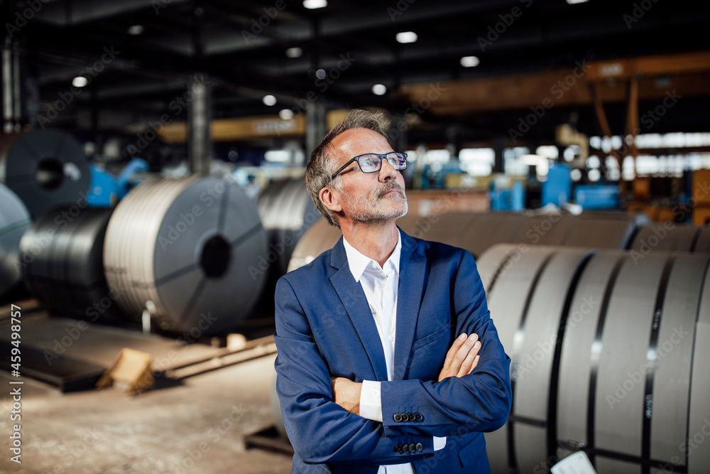Thoughtful businessman with arms crossed standing in warehouse Thoughtful businessman with arms crossed standing in warehouse