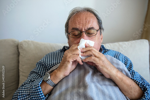 Принти на полотні Elderly unwell man lying on couch at home and blowing nose