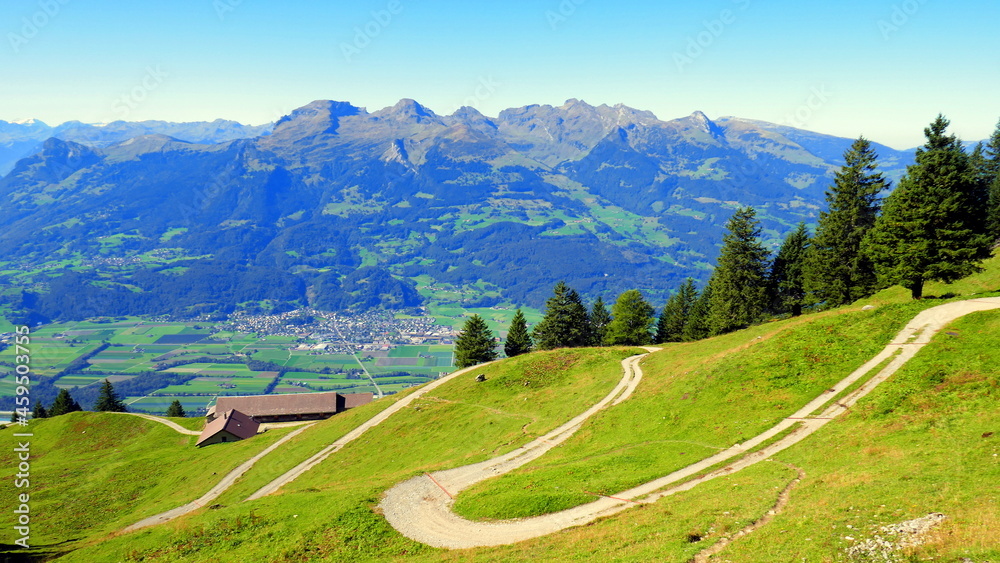 Idyllischer sonniger Wanderweg beim Fürstensteig in Liechtenstein mit grünen Wiesen und hohen Bergen 