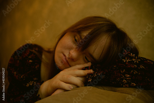 Portrait of young woman with Down Syndrome resting her head on couch and looking sad
