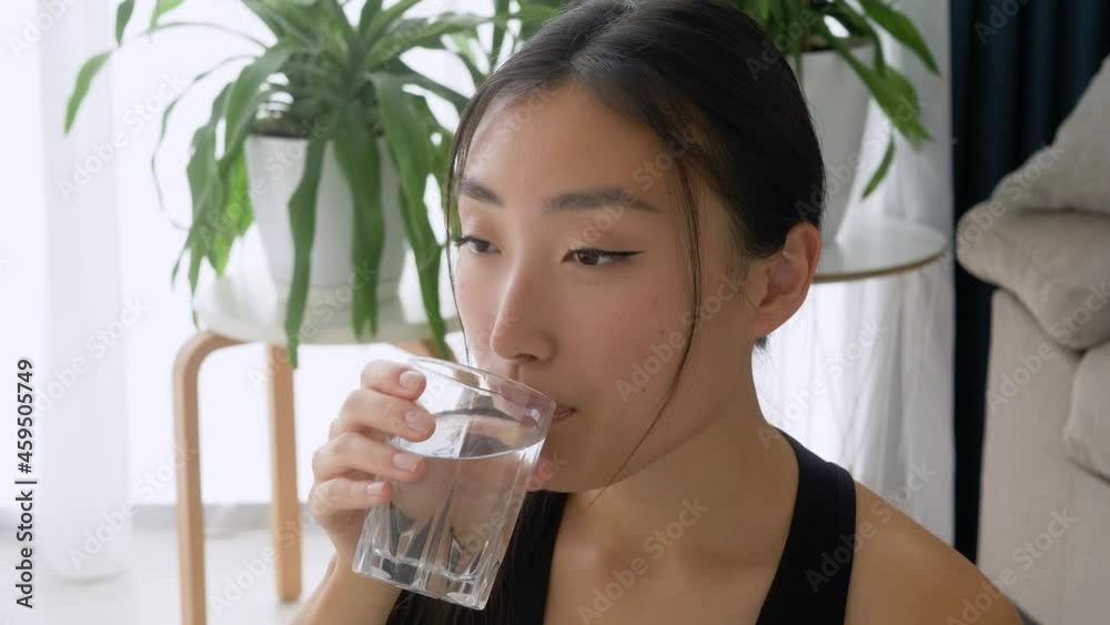 Close-up of pretty asian girl drinking water from glass after home workout exercise at home Close-up of pretty asian girl drinking water from glass after home workout exercise at home
