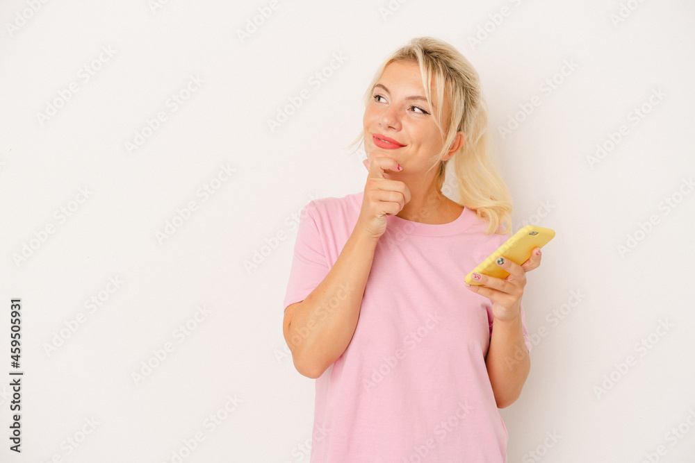 Young Russian woman holding mobile phone isolated on white background looking sideways with doubtful and skeptical expression. Young Russian woman holding mobile phone isolated on white background looking sideways with doubtful and skeptical expression.