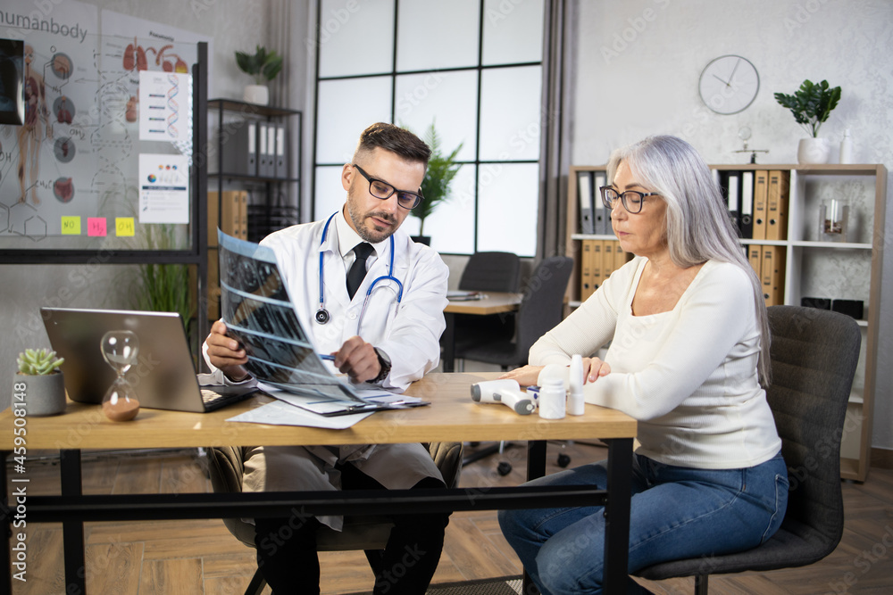 Qualified male doctor explaining results of x ray scan to caucasian aged woman. Female patient having professional consultation at medical center. Health treatment concept.