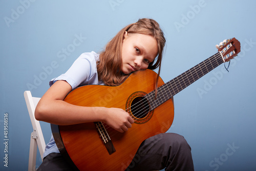 an 11-year-old girl is practicing a melody on a guitar on a blue background