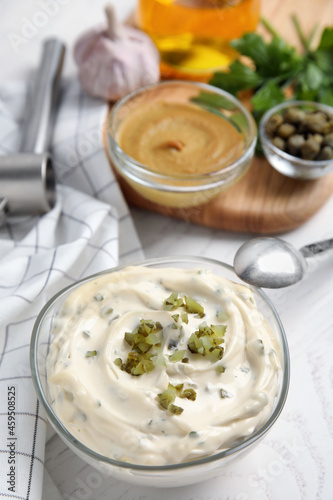 Tasty tartar sauce and ingredients on white table