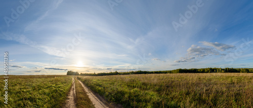 Panorama of a field with a dirt road and a blue sky with the setting sun