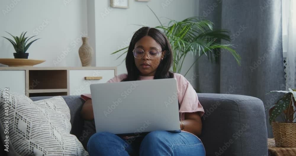 African american woman uses a laptop sitting on a sofa in a modern interior African american woman uses a laptop sitting on a sofa in a modern interior