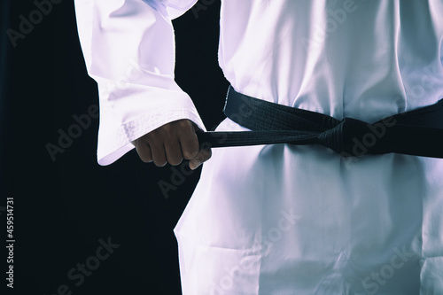 Close up Taekwondo martial arts fighter in white uniform holding black belt on dark background photo