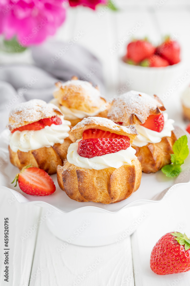 Delicious homemade small cakes profiterole choux pastry with custard, strawberry and icing powder on the white wooden background. Copy space. Delicious homemade small cakes profiterole choux pastry with custard, strawberry and icing powder on the white wooden background. Copy space.