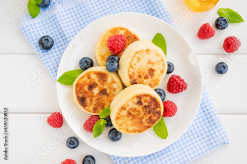 Cottage cheese pancakes with fresh berries, sour cream and honey on a white wooden background. Homemade traditional Ukrainian and Russian syrniki.