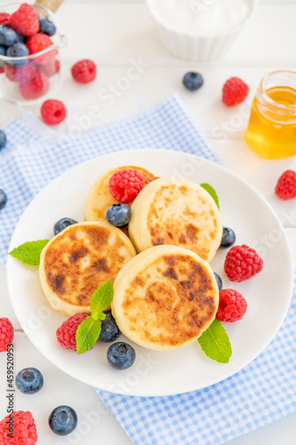 Cottage cheese pancakes with fresh berries, sour cream and honey on a white wooden background. Homemade traditional Ukrainian and Russian syrniki.