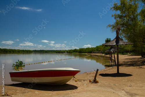 Panorama view of the river beach in a summer sunny day. A boat in the sand in the foreground and the tropical jungle in the background reflected in the water.