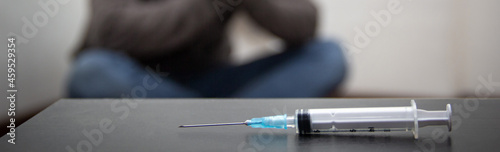 banner of Syringe and man drug addict without of focus sitting in corner in the background