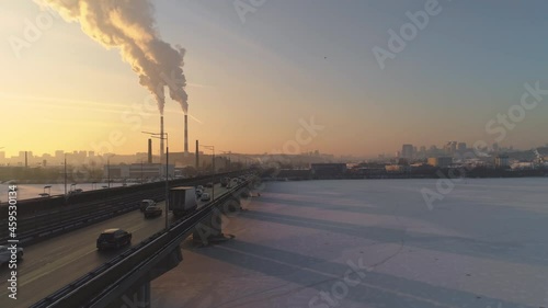 Drone folows cars on frozen bridge at blue and yellow sunset over smoky pipes. Environmental pollution from cars and plant pipes photo