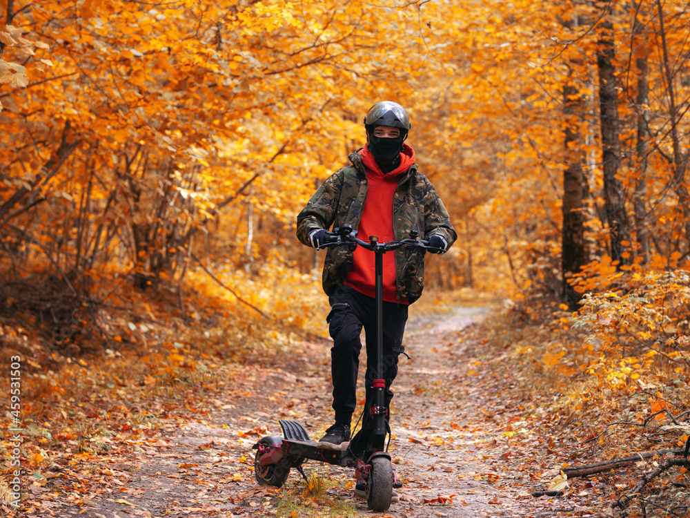 A young man in the autumn forest on an electric scooter. Ride colorful autumn on forest roads.