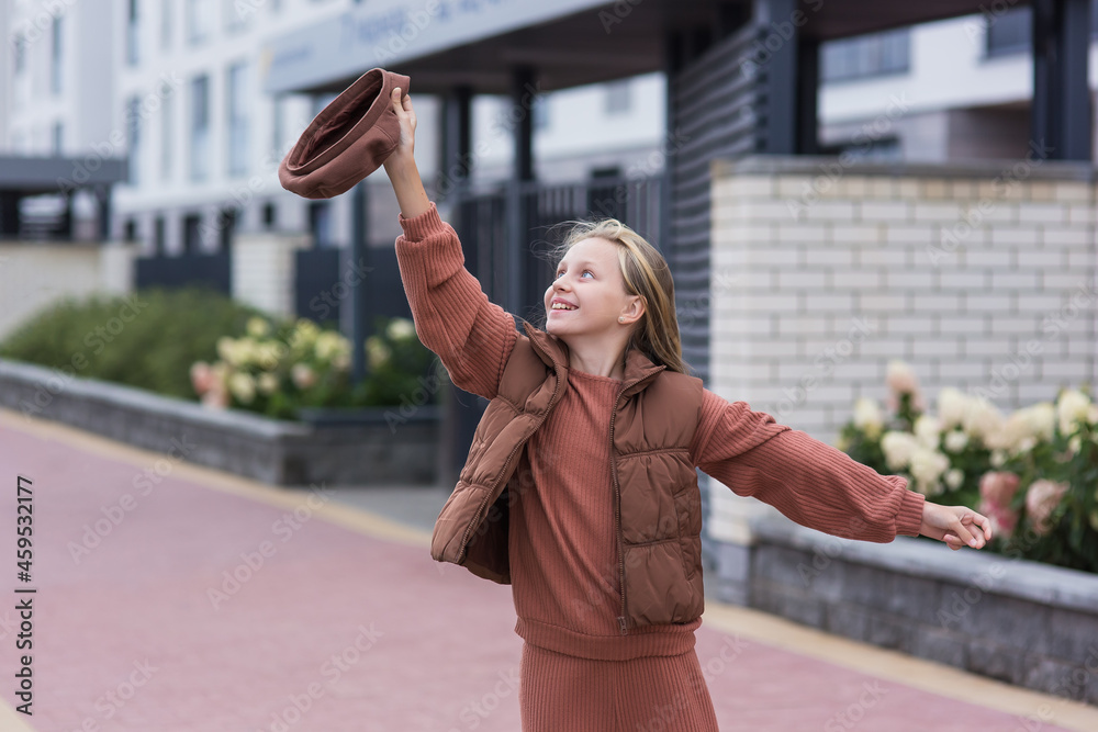 Fototapeta premium A dream come true. Cute caucasian girl in a brown beret and brown clothes shouts cheers while gesturing with her hand on a city street
