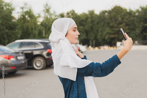 Young Arab student girl wearing a headscarf making selfie on her smartphone outdoors.