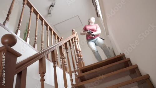 Caucasian woman in a red T-shirt descends the stairs with a rifle in her hands. Self defense concept. Middle aged woman holding a riffle.