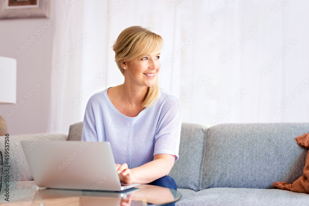 Blond haired middle aged woman working laptop while sitting on a couch Blond haired middle aged woman working laptop while sitting on a couch