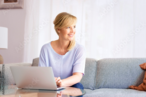 Blond haired middle aged woman working laptop while sitting on a couch