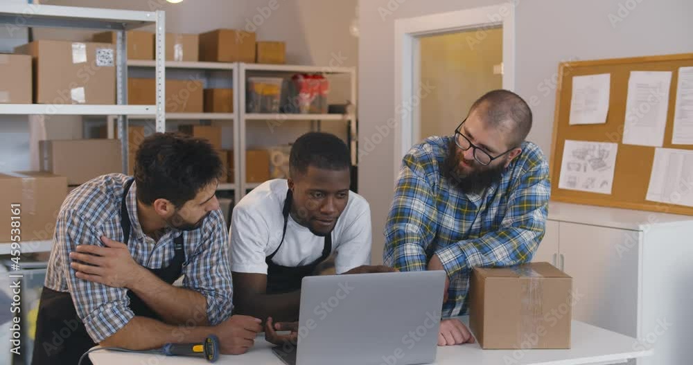 Diverse small business owners discuss idea on laptop in warehouse. Diverse small business owners discuss idea on laptop in warehouse.