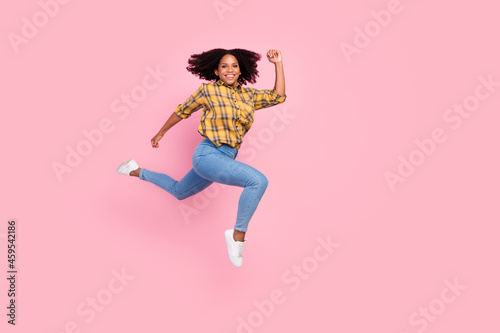 Photo of cheerful hurry lady jump run fast wear checkered shirt jeans footwear isolated pink color background