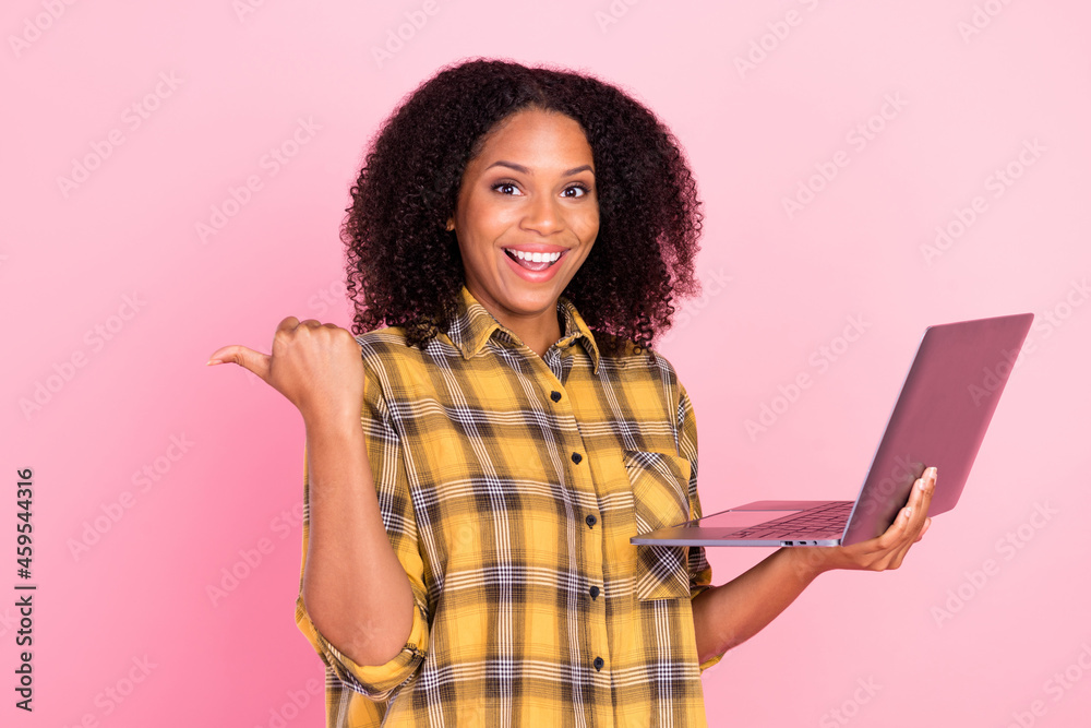 Photo of charming pretty dark skin lady wear checkered shirt pointing thumb empty space holding gadget isolated pink color background