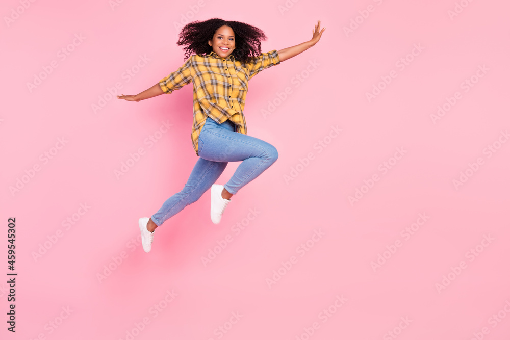 Photo of cheerful inspired lady jump have fun wear plaid shirt jeans sneakers isolated pink color background