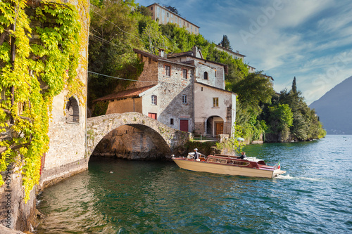 Fashioned touristic wooden speedboat approaching an old stone bridge at Lake Como