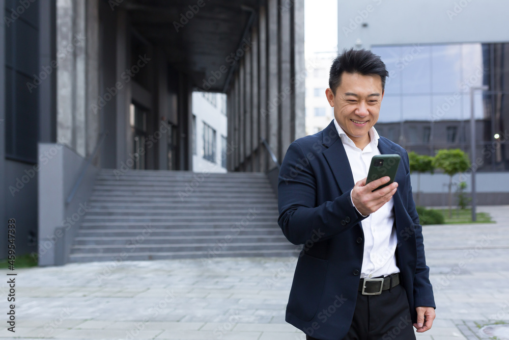 Portrait of Asian cheerful and successful businessman near office in business suit got good news read good news online Portrait of Asian cheerful and successful businessman near office in business suit got good news read good news online