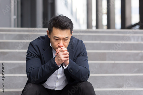 Asian office worker manager tired after work sitting on office stairs, dissatisfied with work result photo