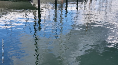 Water level reflecting the masts of sailboats, port moorings and blue sky with white clouds